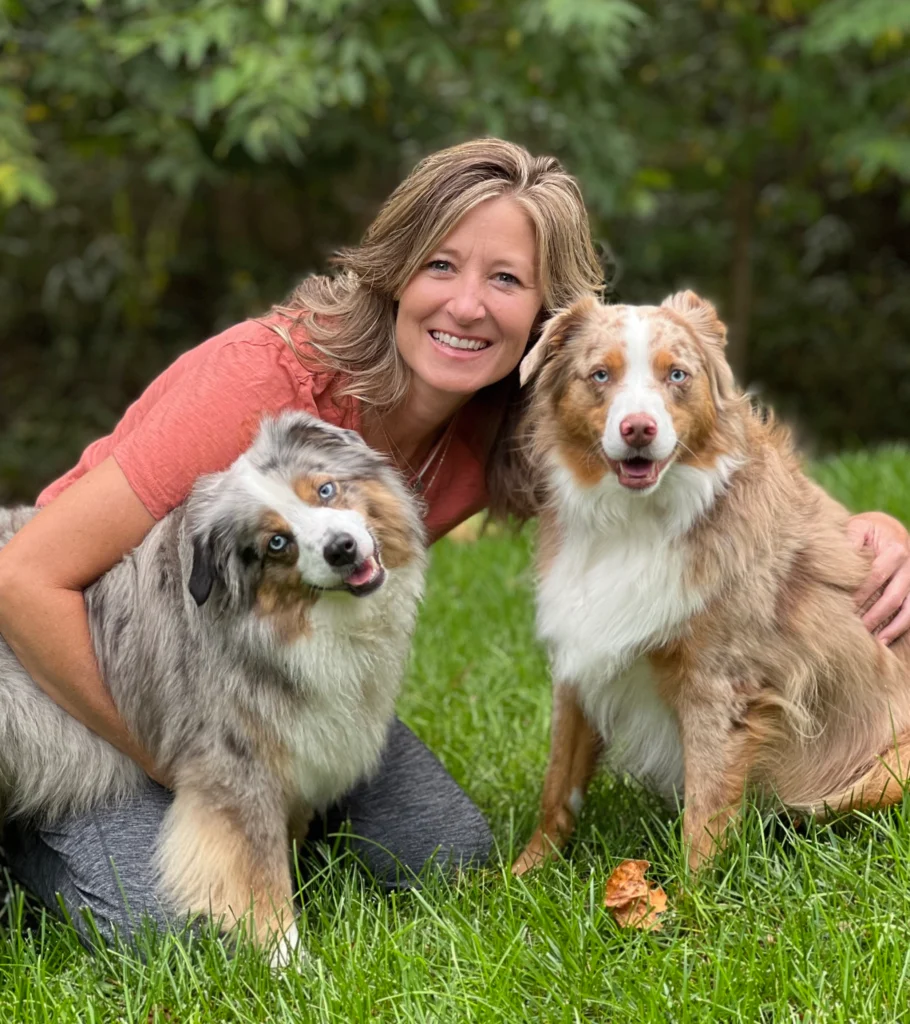 A woman and two dogs sitting in the grass.