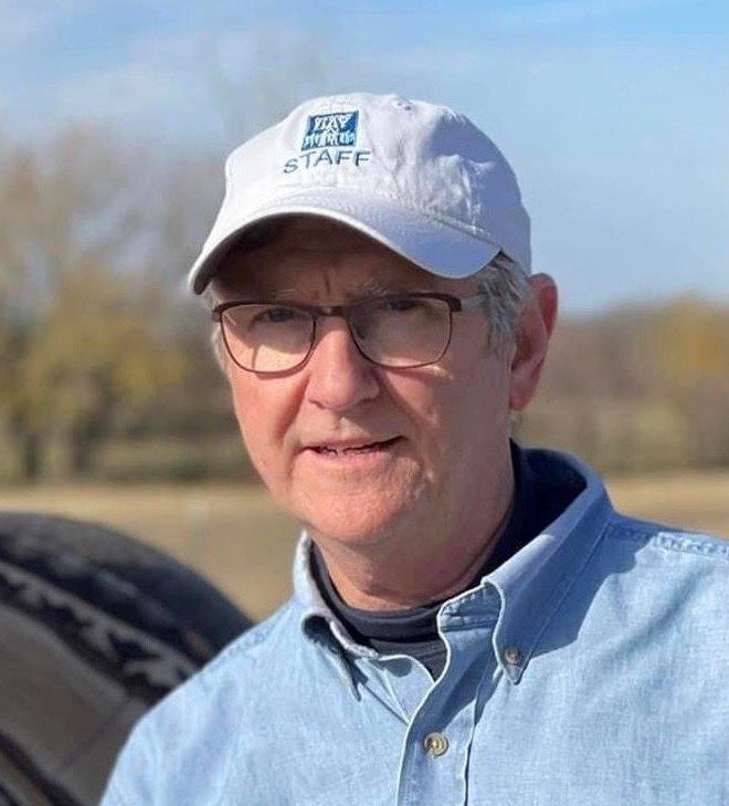 A man wearing glasses and a hat standing in front of a tire.