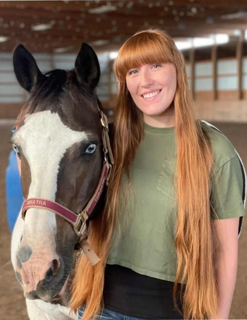 A woman standing next to a horse in an arena.