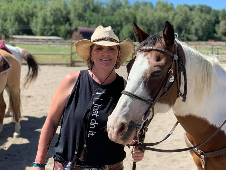 A woman standing next to a horse in the dirt.