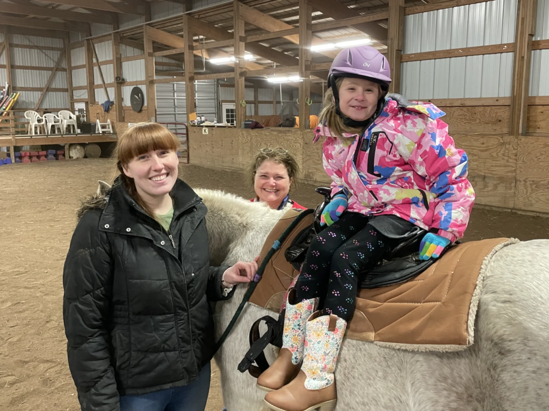 Three women are sitting on a horse in an indoor arena.