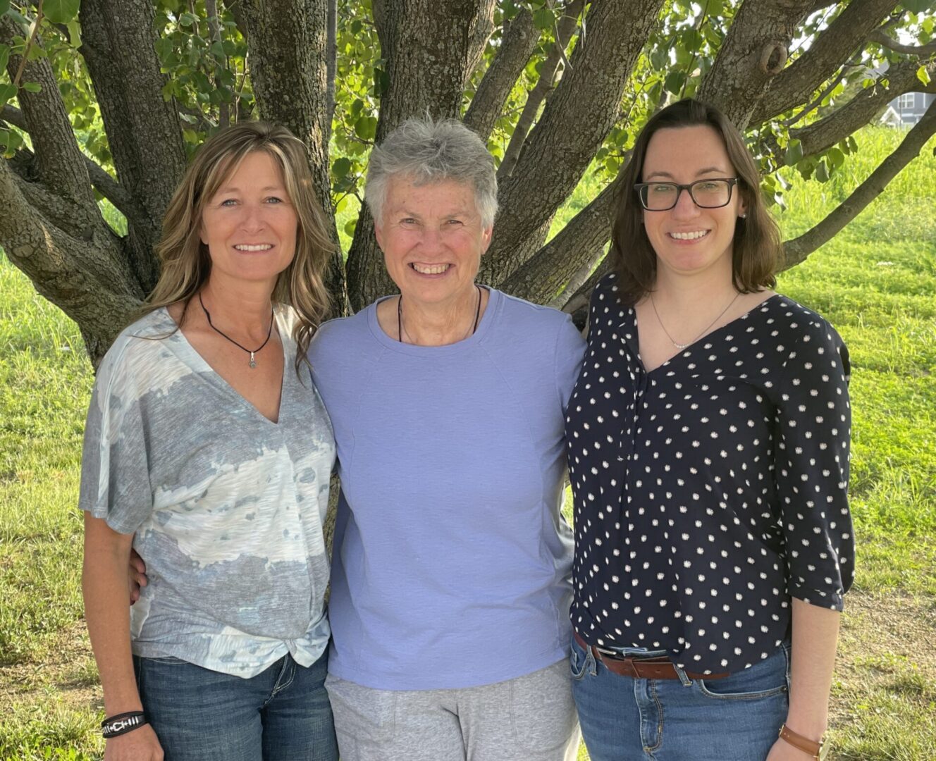 Three women standing next to each other under a tree.